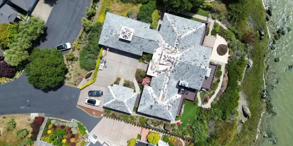 Aerial view of a large waterfront home with a complex gray shingle roof in Sacramento