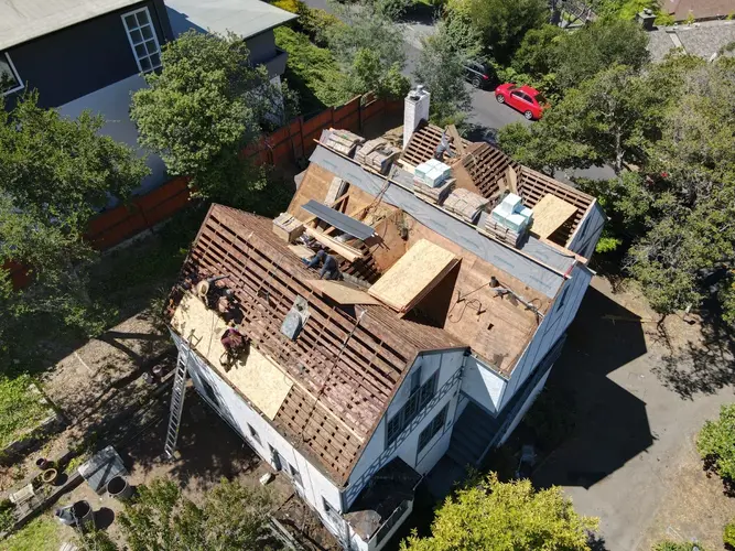 Milpitas home undergoing roof replacement with exposed wooden decking and roofing materials staged on top
