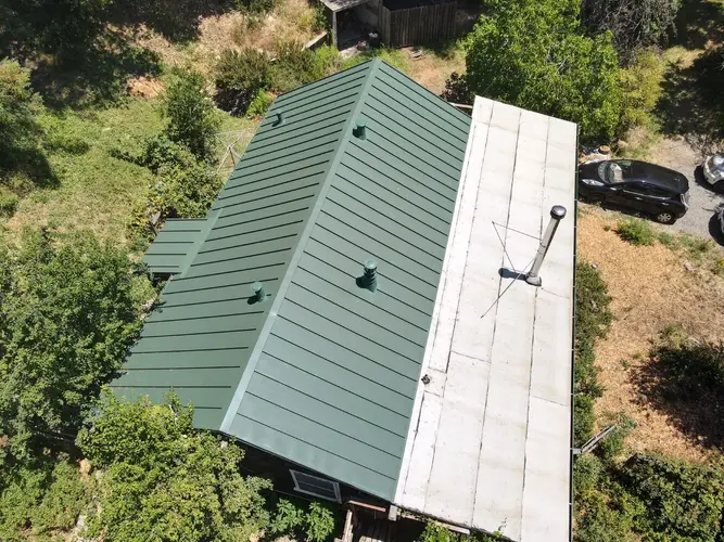 Modern green standing seam metal roof installed on a residential home with surrounding greenery, showcasing energy-efficient and durable roofing solution